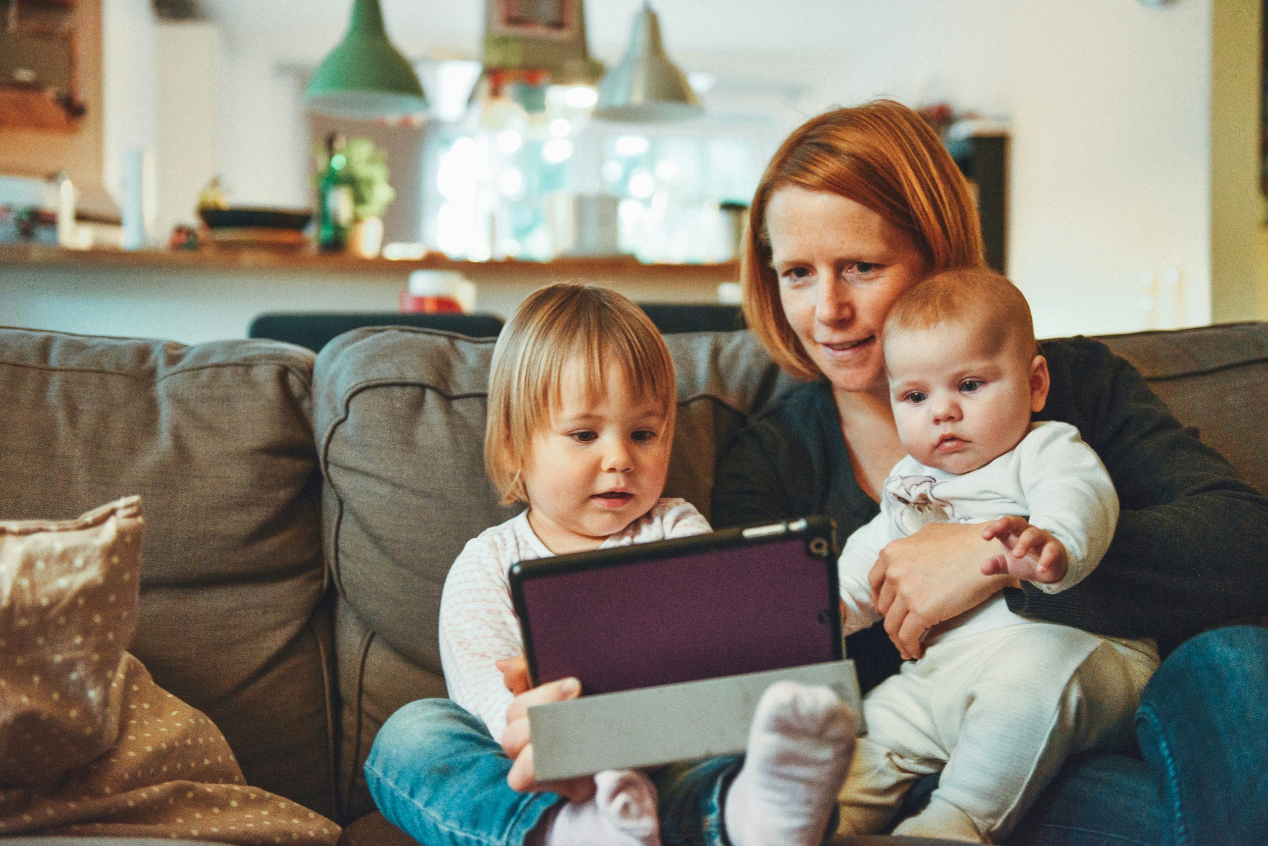 mom holding two kids all of them looking at an ipad