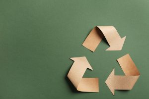 Recycling symbol cut out of kraft paper on green background, top view.