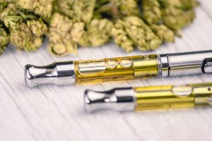 THC/CBD cannabis vape pens up-close with marijuana leaf on white