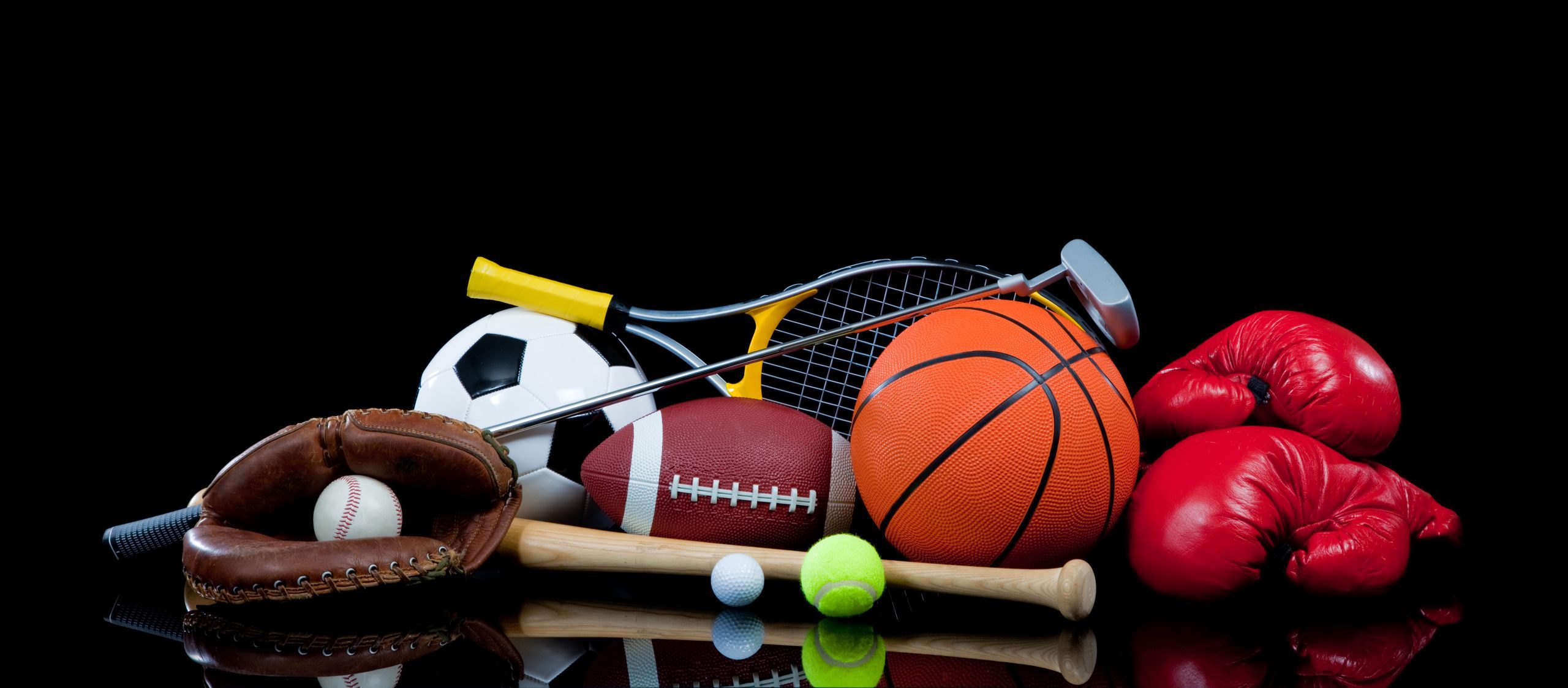 A group of sports equipment on black background including tennis, basketball, baseball, american fotball and soccer and boxing equipment on a black background with copy space